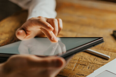 Close up photo of male hands tapping on digital tablet screen.