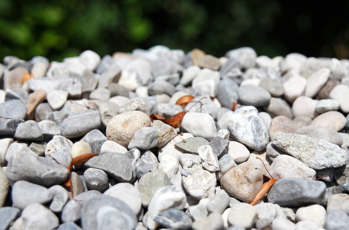 Kies - Steine in verschiedenen Größen und Farben auf einem Haufen, dazwischen finden sich einige welke Blätter