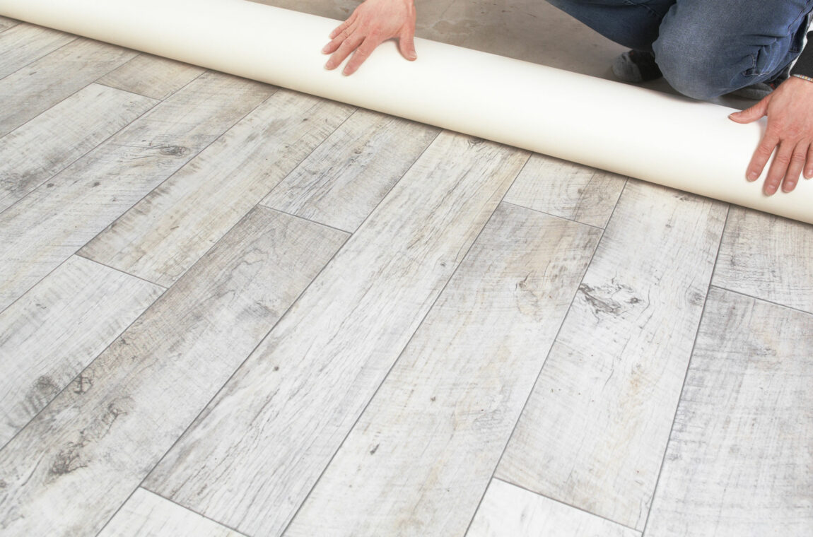 Ein PVC Fußbodenbelag in grau-weißer Holzoptik wird ausgerollt