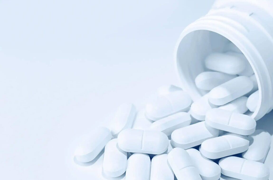 Anwendungen: Pharmazeutika: Tablettendose liegt auf der Seite, eine kleine Menge weißer Tabletten mit Bruchkerbe ist aus der Dose gefallen und liegt in der Öffnung